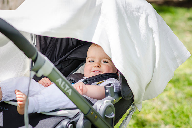 Smiling baby in pram under a white musluv cover