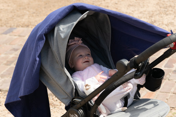 Baby smiling in pram covered by dark musluv cover