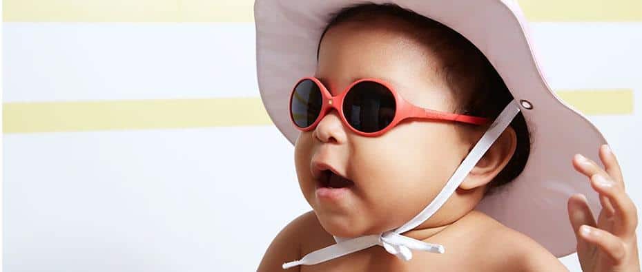 Baby wearing red baby sunglasses and a hat smiling