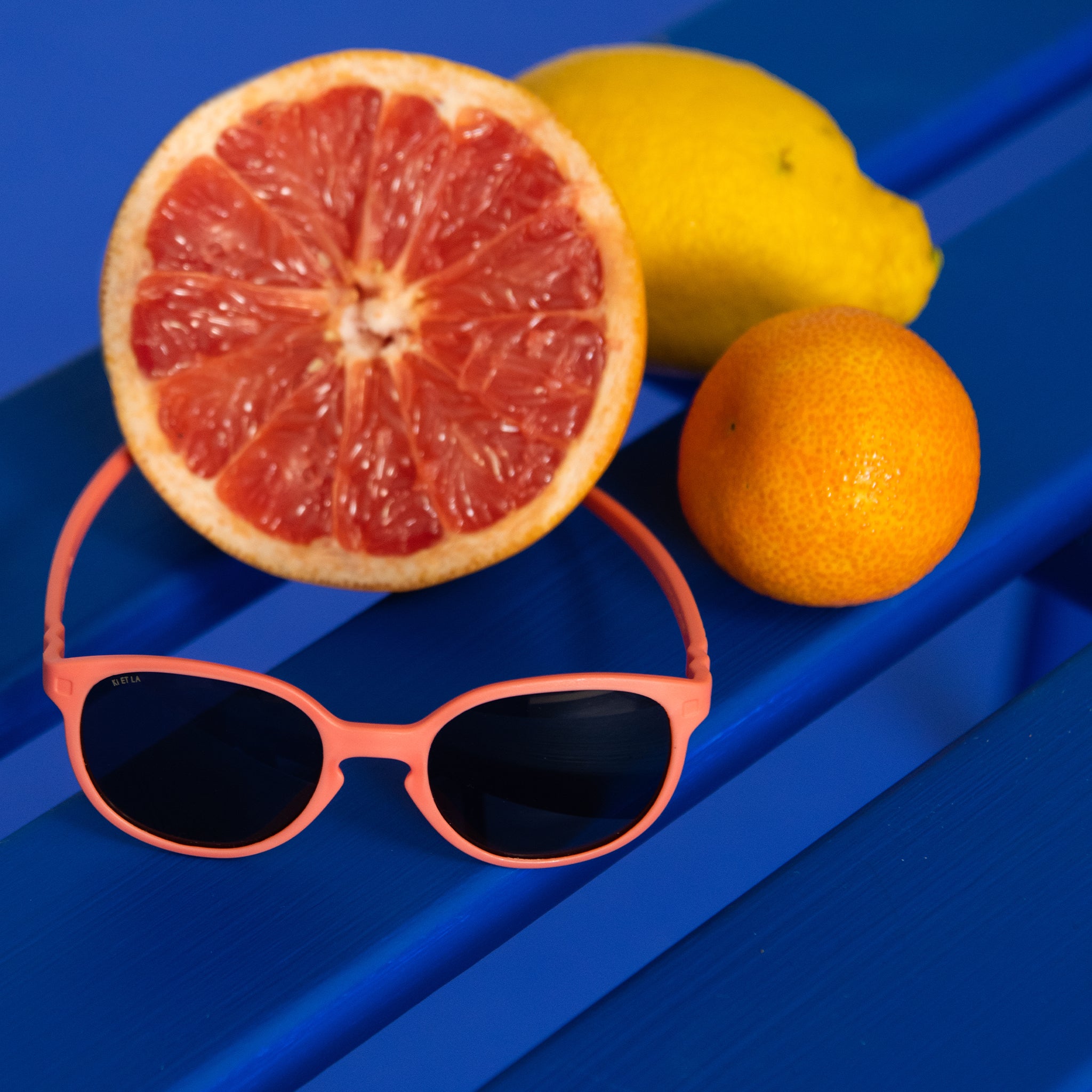Pink todder sunglasses on a royal blue background with citrus fruits